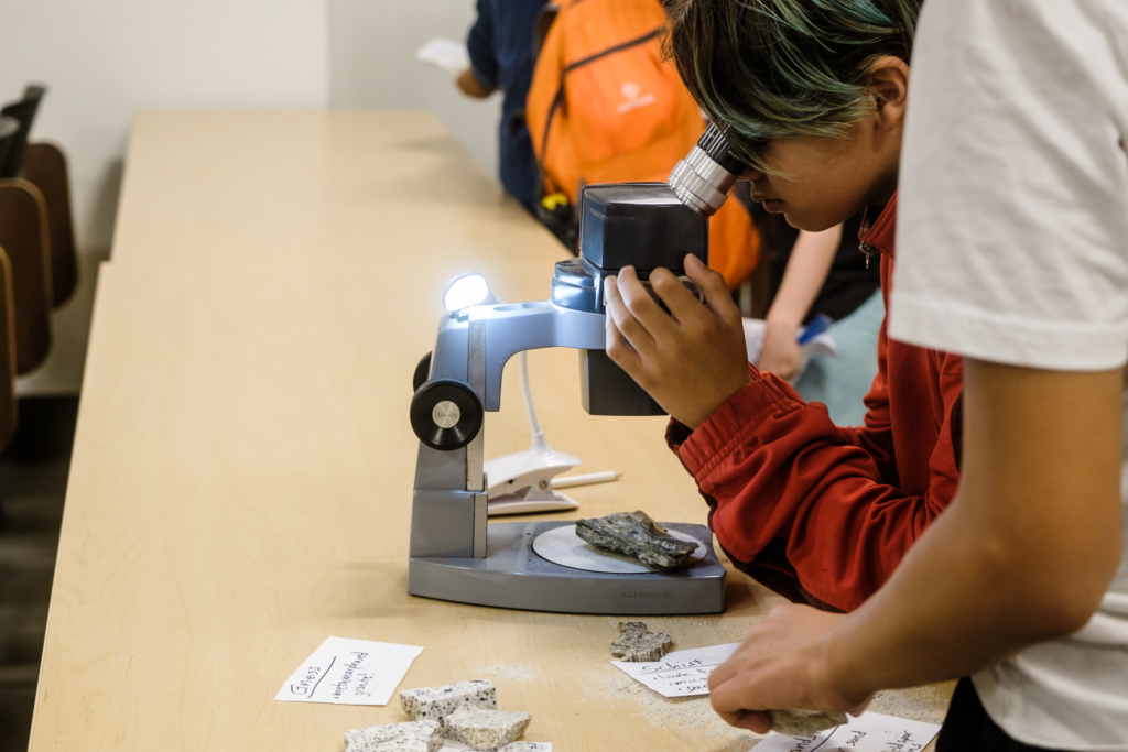 Child peers at rocks under a microscope at EPSS's EYU 2022 booth on Rocks of Southern California.